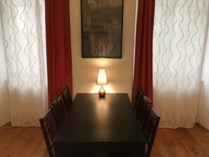 A dining area with a table, chairs, a lamp, and curtains.