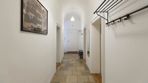 A hallway with a tiled floor, a framed picture on the left wall, a coat rack on the right, and a door at the end. - Heart of Vienna Home (Vienna)