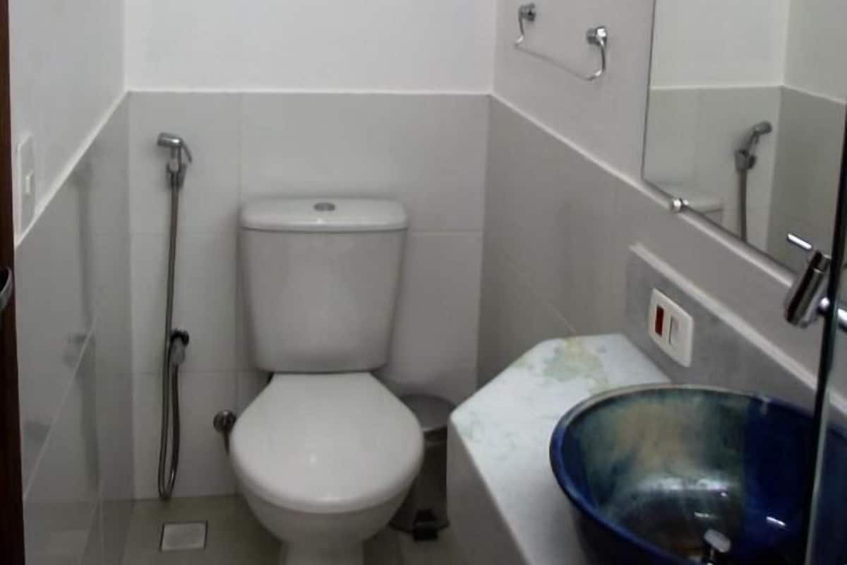 A small, white bathroom with a toilet, a shower, and a sink with a blue basin.