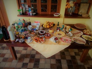 A table with various food items and condiments, including fruits, pastries, and bottles. - Pousada Miracolo (Paraty)