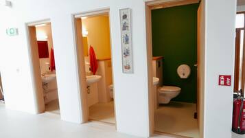 Un pasillo con tres puertas que dan a distintas habitaciones, cada una con lavamanos e inodoro.