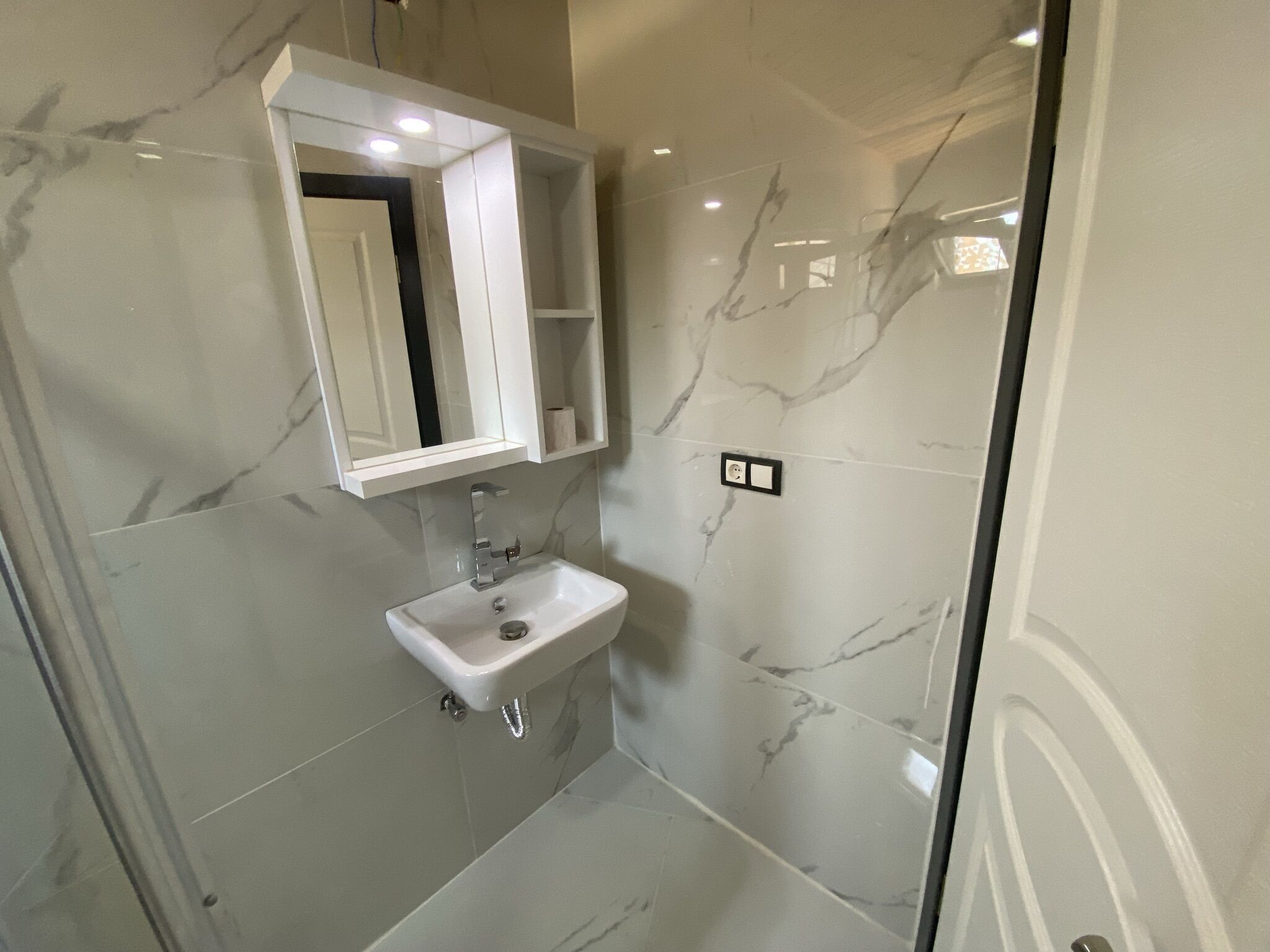 A bathroom with a white sink, a mirror, and a marble-tiled wall.