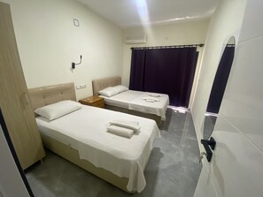 Quarto de hotel com duas camas, uma mesa de cabeceira de madeira, um espelho e uma janela com cortinas.