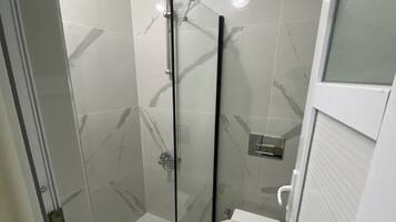 Un baño moderno con cabina de ducha de vidrio, inodoro y lavamanos.