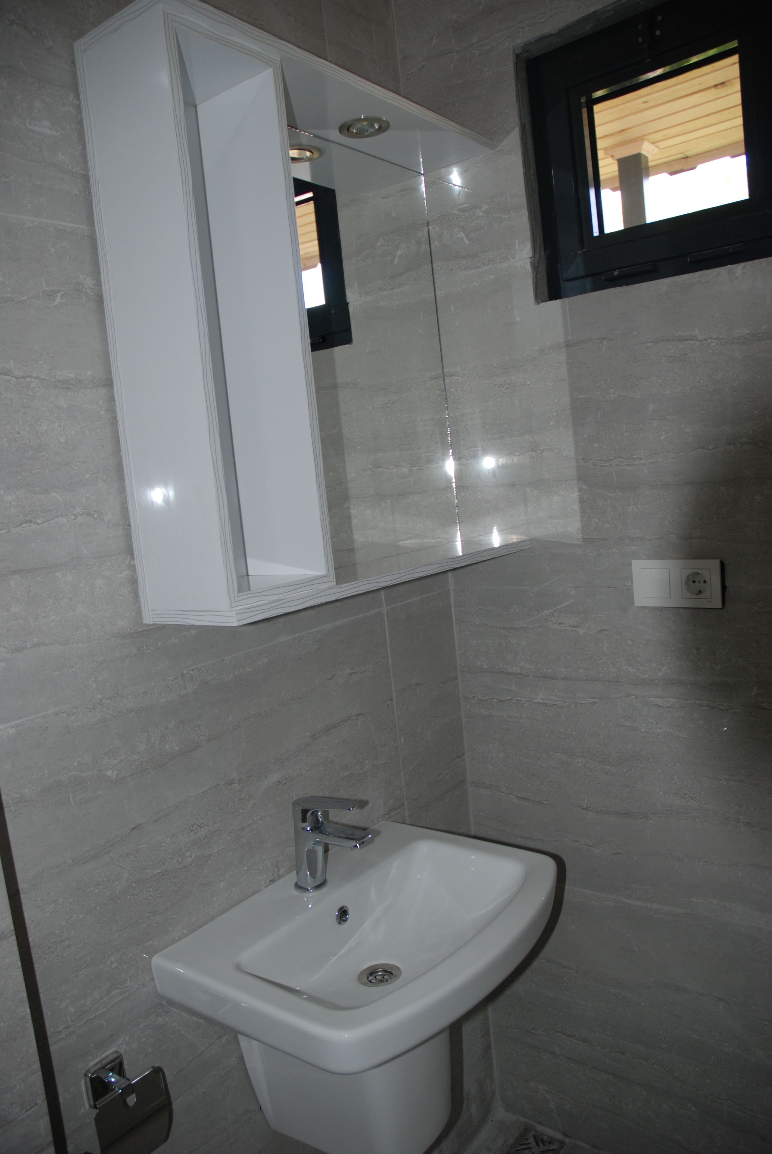Un baño con lavamanos blanco, un espejo y una ventana.