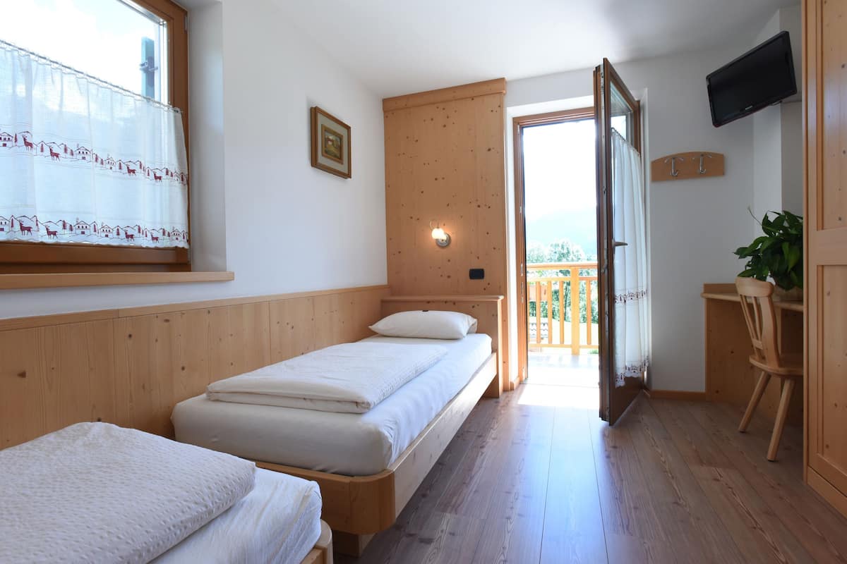 Een kamer met twee eenpersoonsbedden, een houten plafond, een aan de muur bevestigde televisie en een balkon met een houten hekwerk.