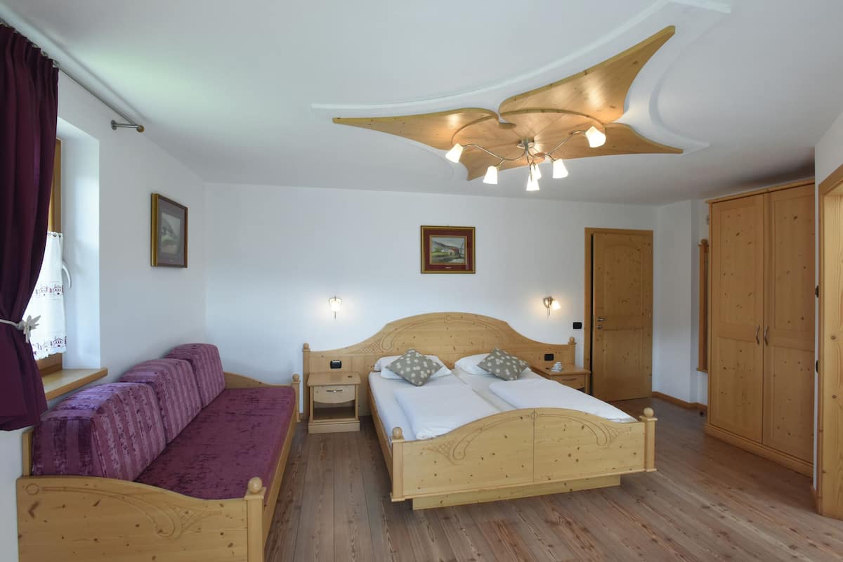 Een slaapkamer met een houten bed, een houten bankje, een plafondventilator en een kledingkast.