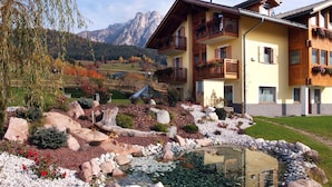 A hotel with a mountain view, a garden with a pond, and a ski lift in the background.