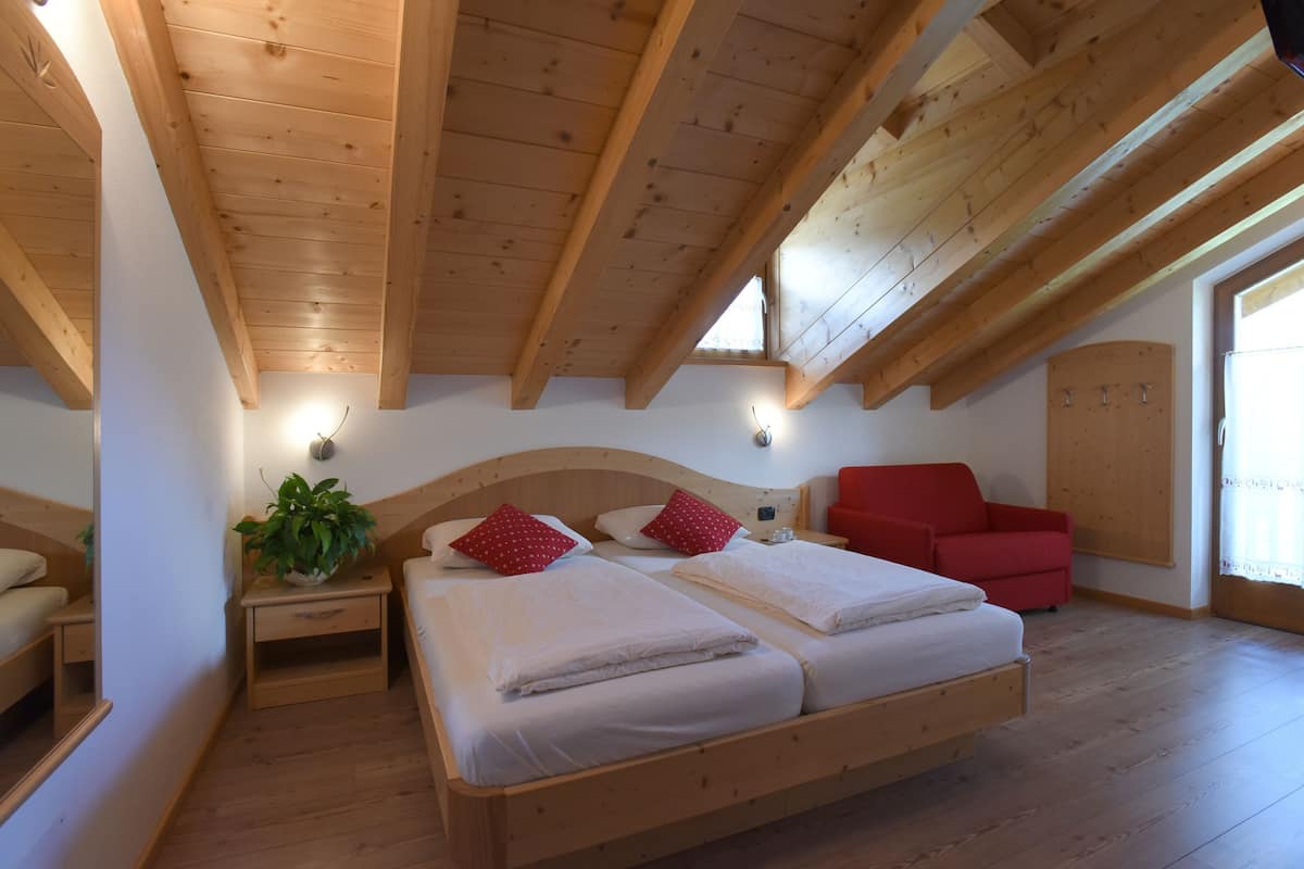 Een slaapkamer met een houten plafond, een bed met witte lakens, een rode stoel en een nachtkastje met een plant.