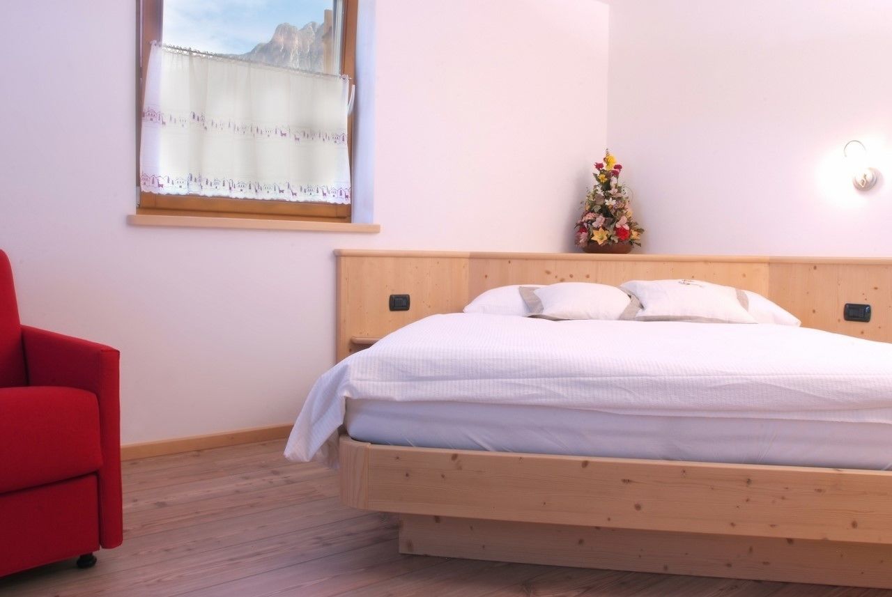 A bedroom with a wooden bed, a red chair, a window with a view, and a small flower arrangement on the nightstand.