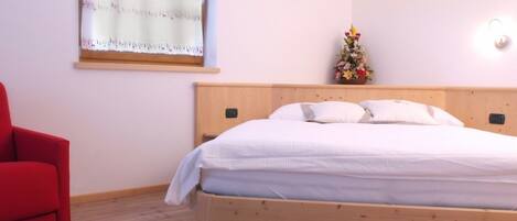 A bedroom with a wooden bed, a red chair, a window with a view, and a small flower arrangement on the nightstand.