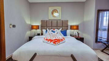 Een hotelkamer met een groot bed, een hoofdeinde, nachtkastjes met lampen, een lijst met een afbeelding aan de muur, en een raam met gordijnen.