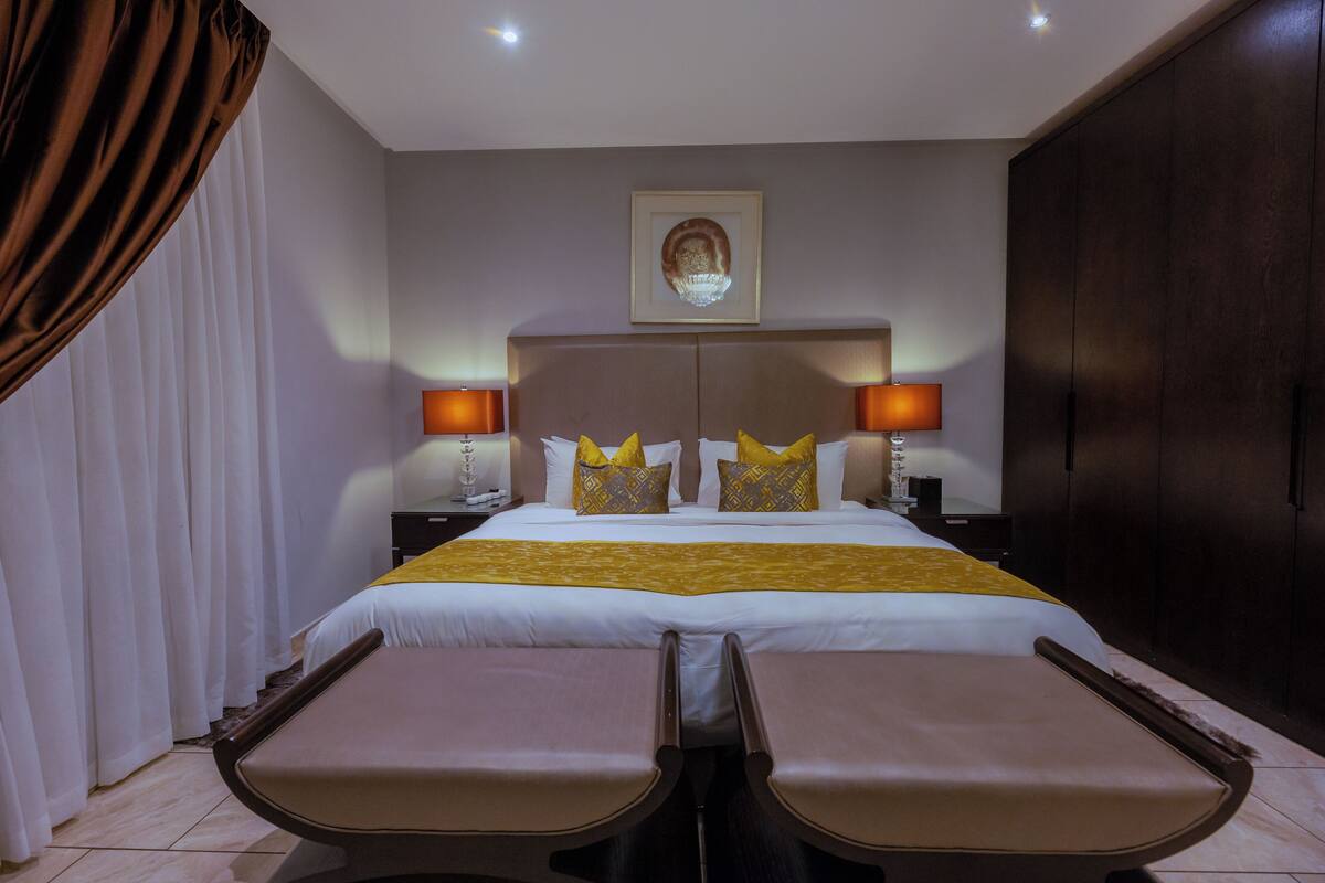 A hotel room with a large bed, two bedside tables, a headboard, a chandelier, and a large wardrobe.