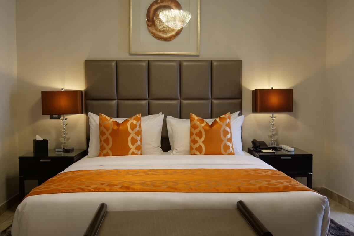A hotel room with a large bed, two bedside tables, a headboard, and a framed artwork above the bed.