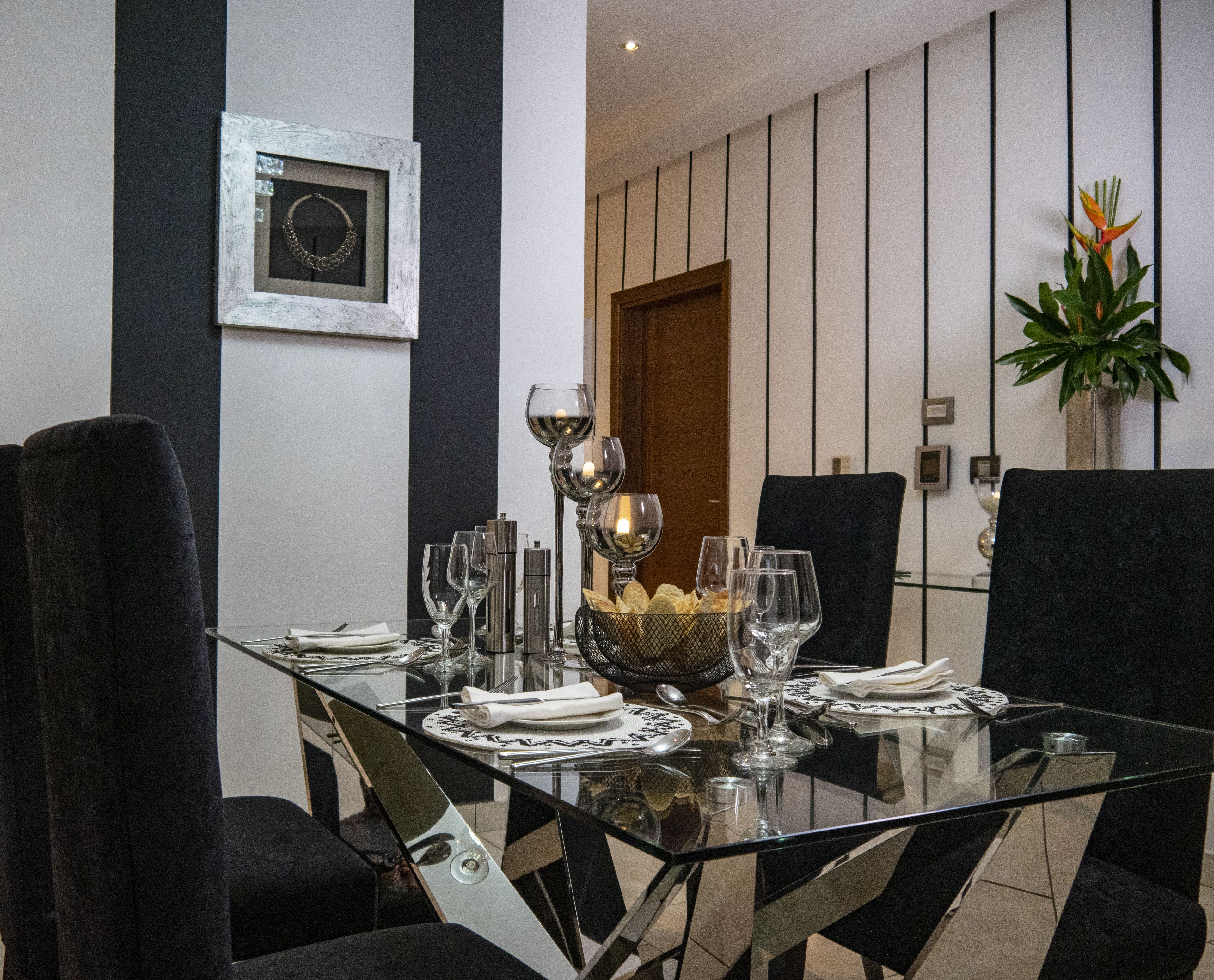 A modern dining room with a glass table set for six, black upholstered chairs, and a decorative wall piece.