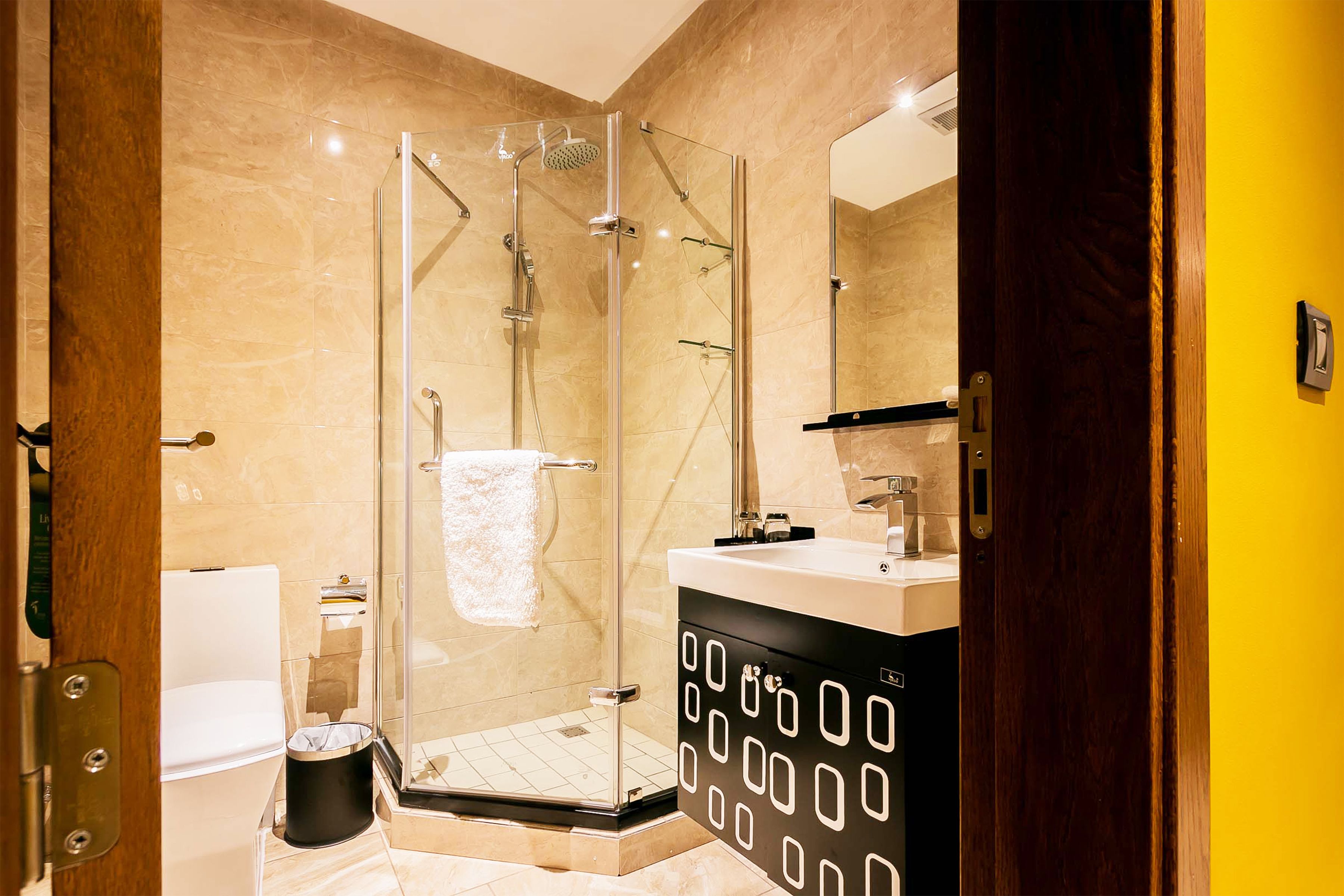 A modern bathroom with a glass-enclosed shower, a white toilet, and a black sink with a geometric design.