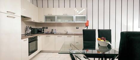 Una cocina moderna con armarios blancos, una mesa de comedor de vidrio y sillas negras.