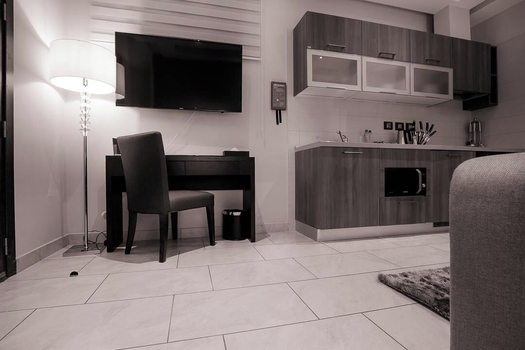 A modern kitchen with a flat-screen TV above the counter, a dining area with a chair and table, and a small rug on the floor.