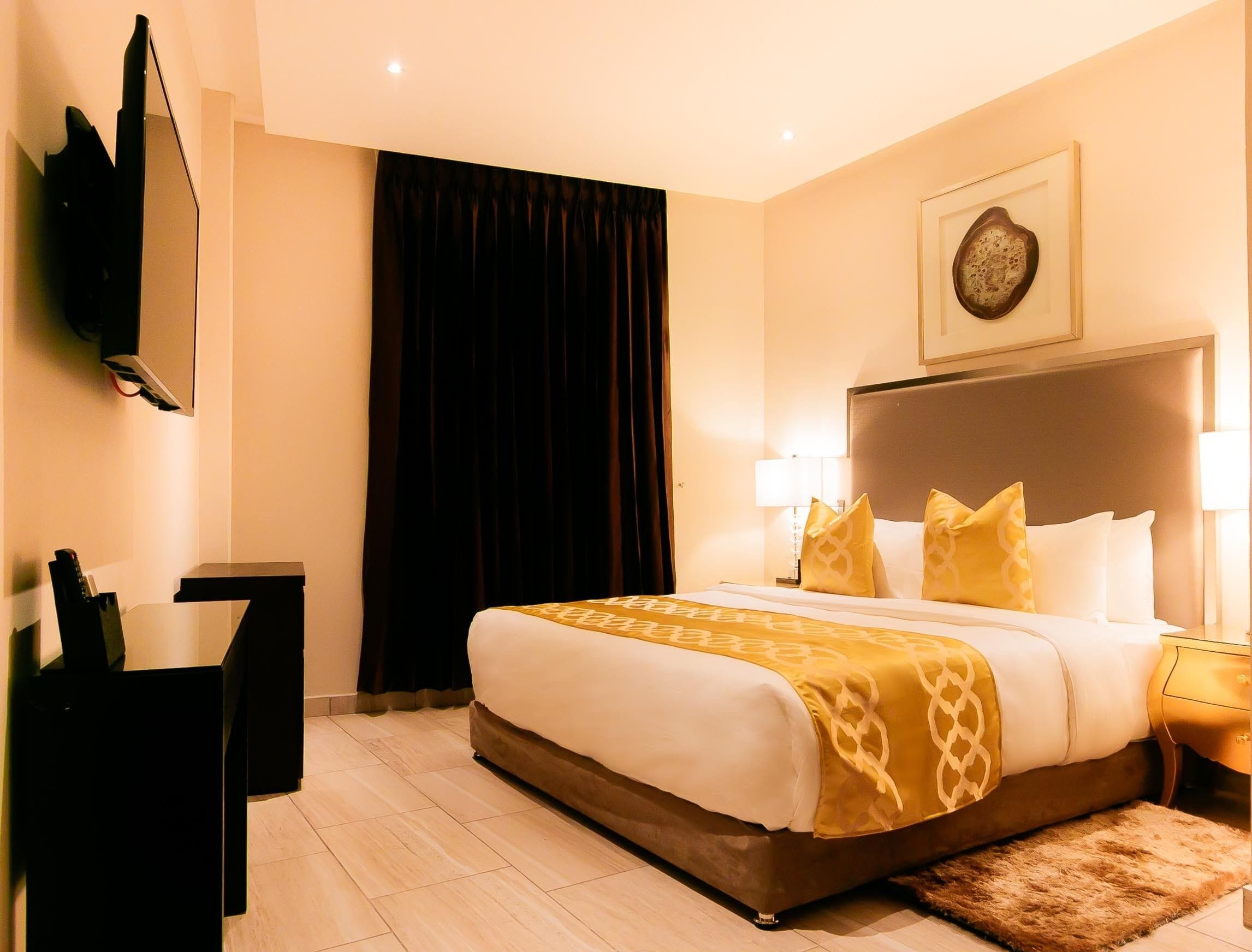 A hotel room with a large bed, a desk, a flat-screen TV, a lamp, and a framed picture on the wall.