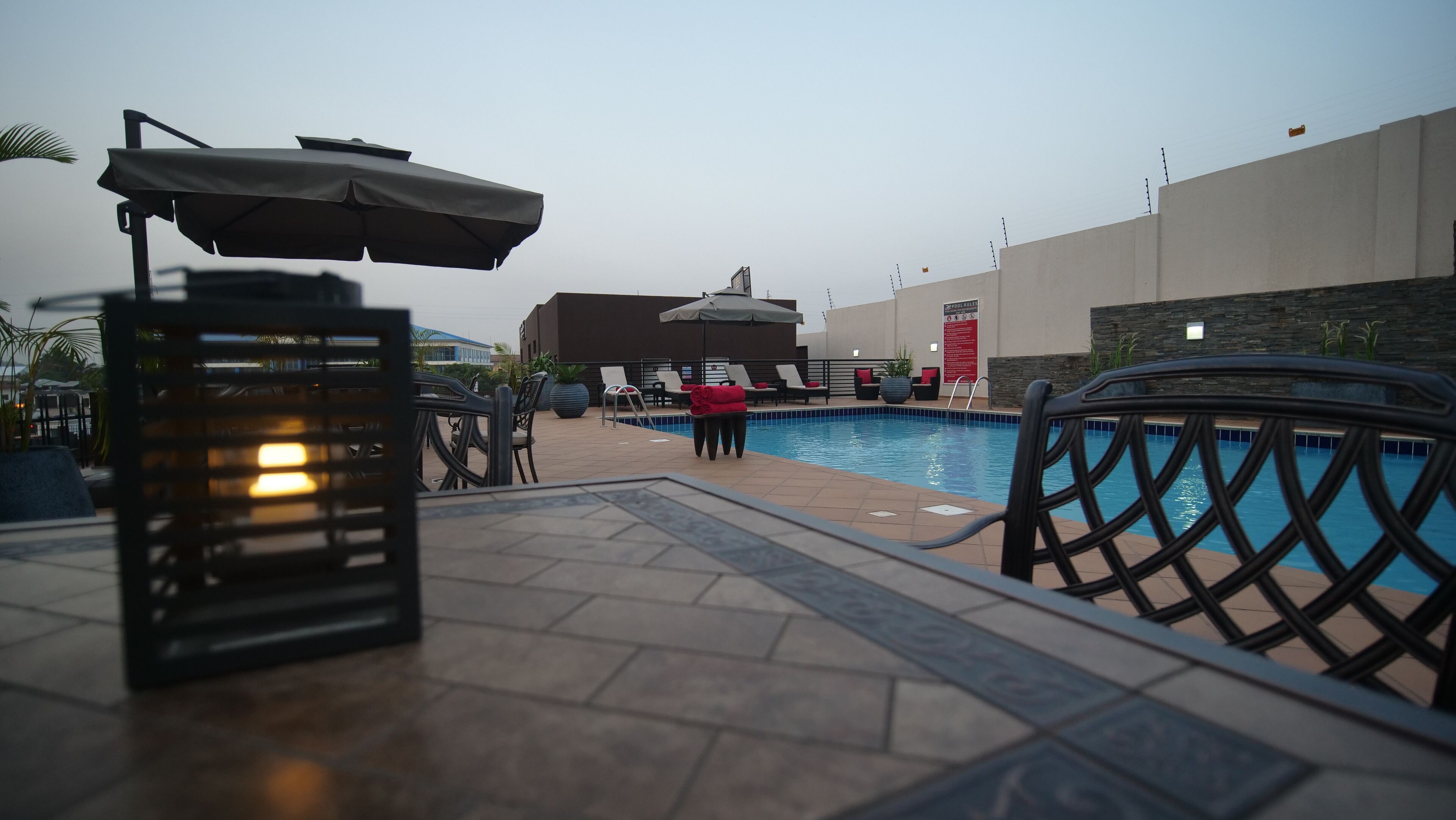 A poolside area with lounge chairs, an umbrella, and a pool.