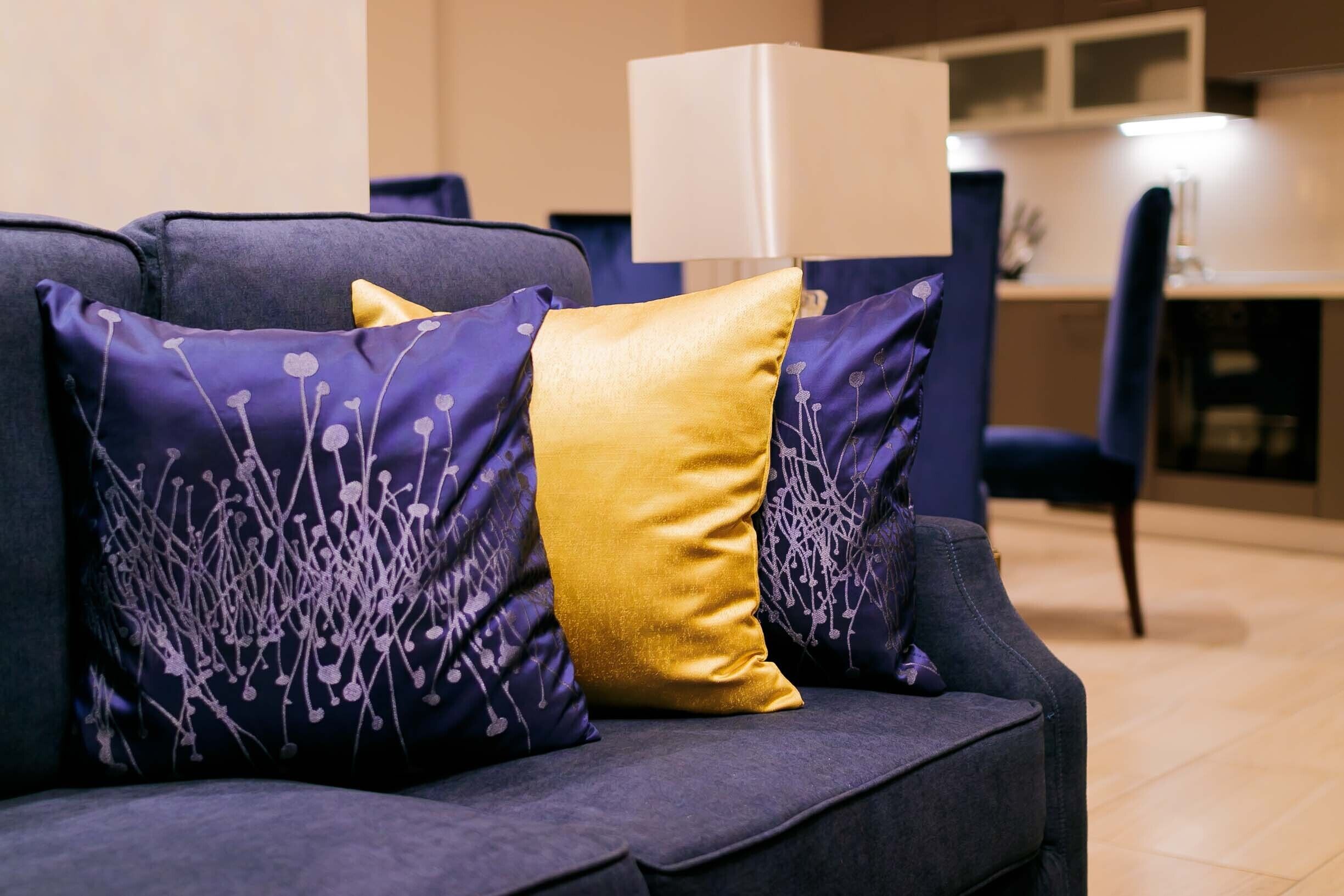 A dark blue sofa with two decorative pillows, one gold and one purple with a floral pattern.