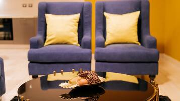 Un salon moderne avec deux fauteuils bleus, une table basse en verre agrémentée d’objets décoratifs et un mur jaune en arrière-plan.