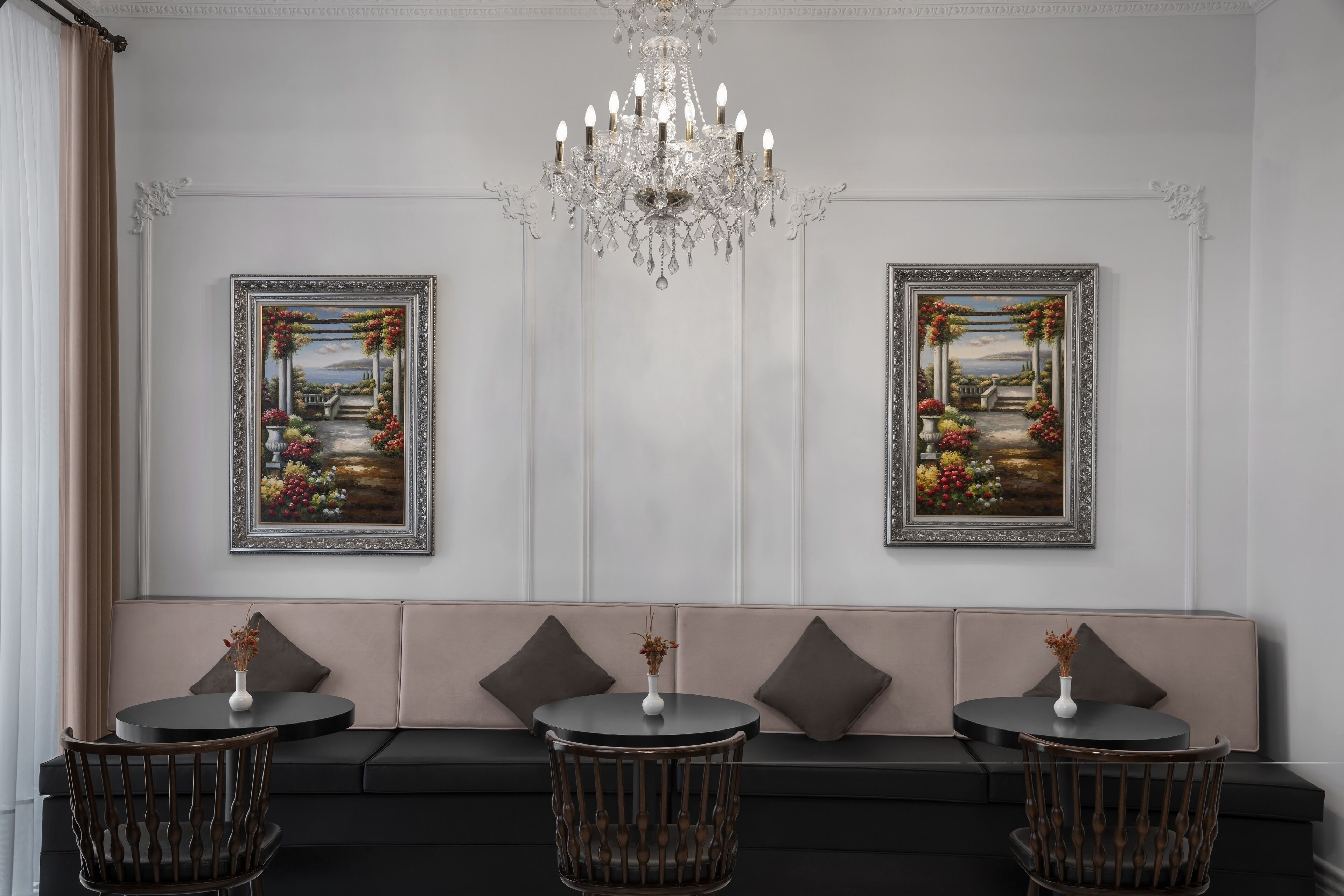 Een kamer met een zwarte bank, twee ronde tafels en twee inlijste schilderijen aan de muur.