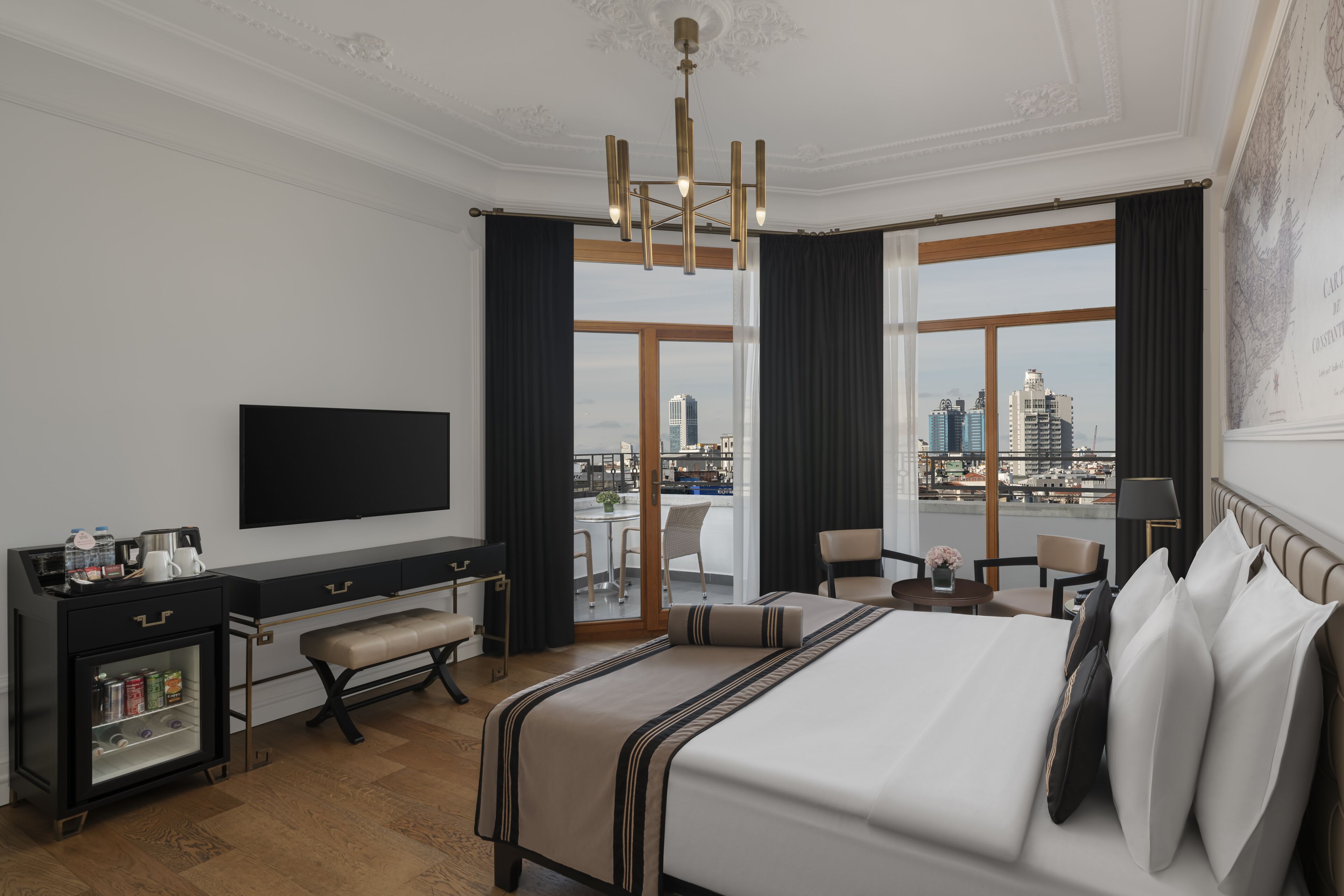A hotel room with a large bed, a desk, a flat-screen TV, and a city view through large windows.