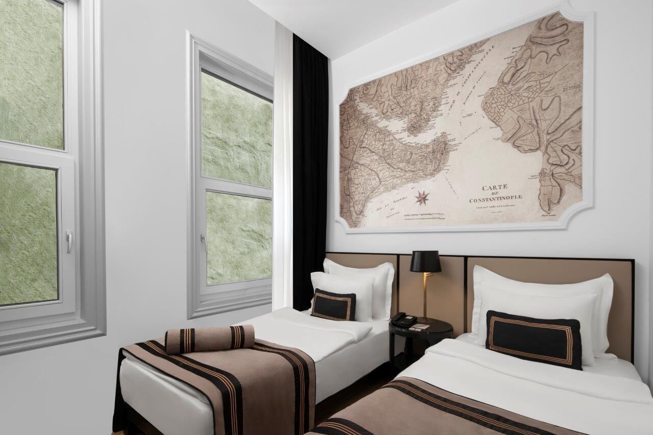 A hotel room with two beds, a large map on the wall, and a view of the outdoors through the windows.
