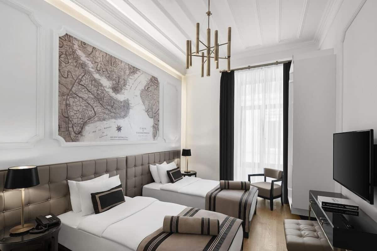 A hotel room with two beds, a large map on the wall, a TV, and a chandelier.