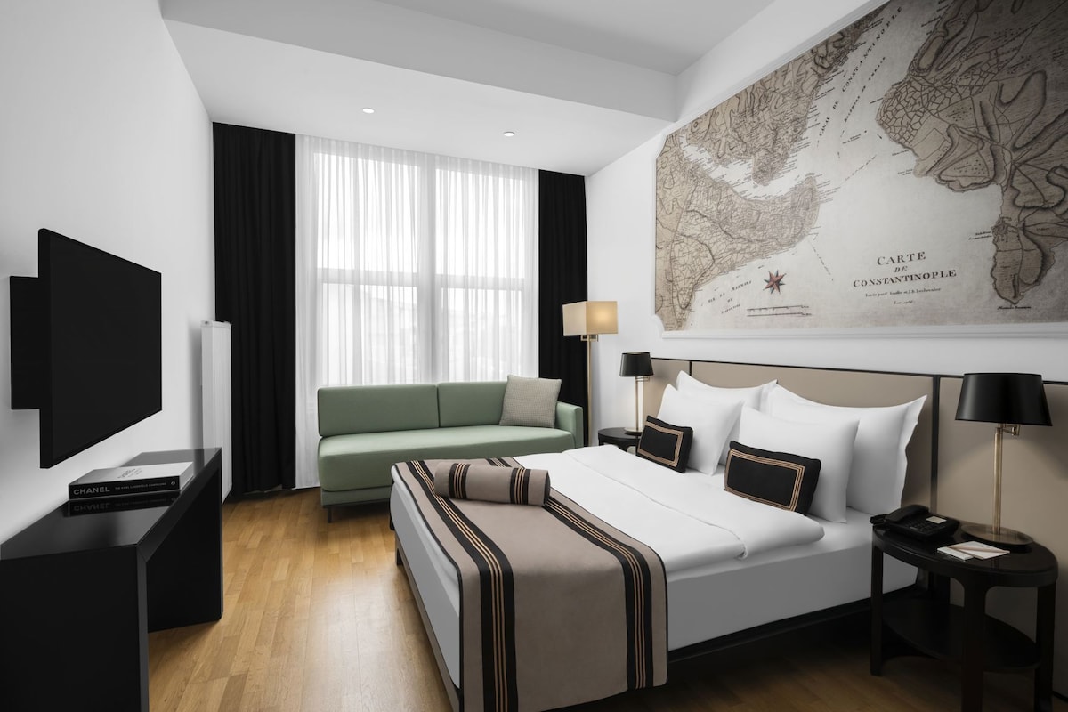 A modern hotel room with a bed, a green sofa, a TV, and a map on the wall.