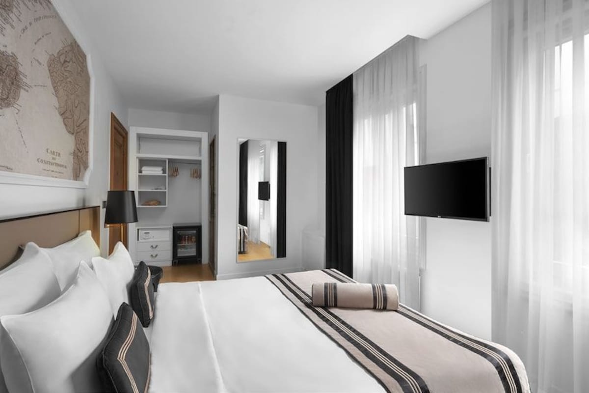 A hotel room with a large bed, a flat-screen TV, a map on the wall, and a desk with a chair.