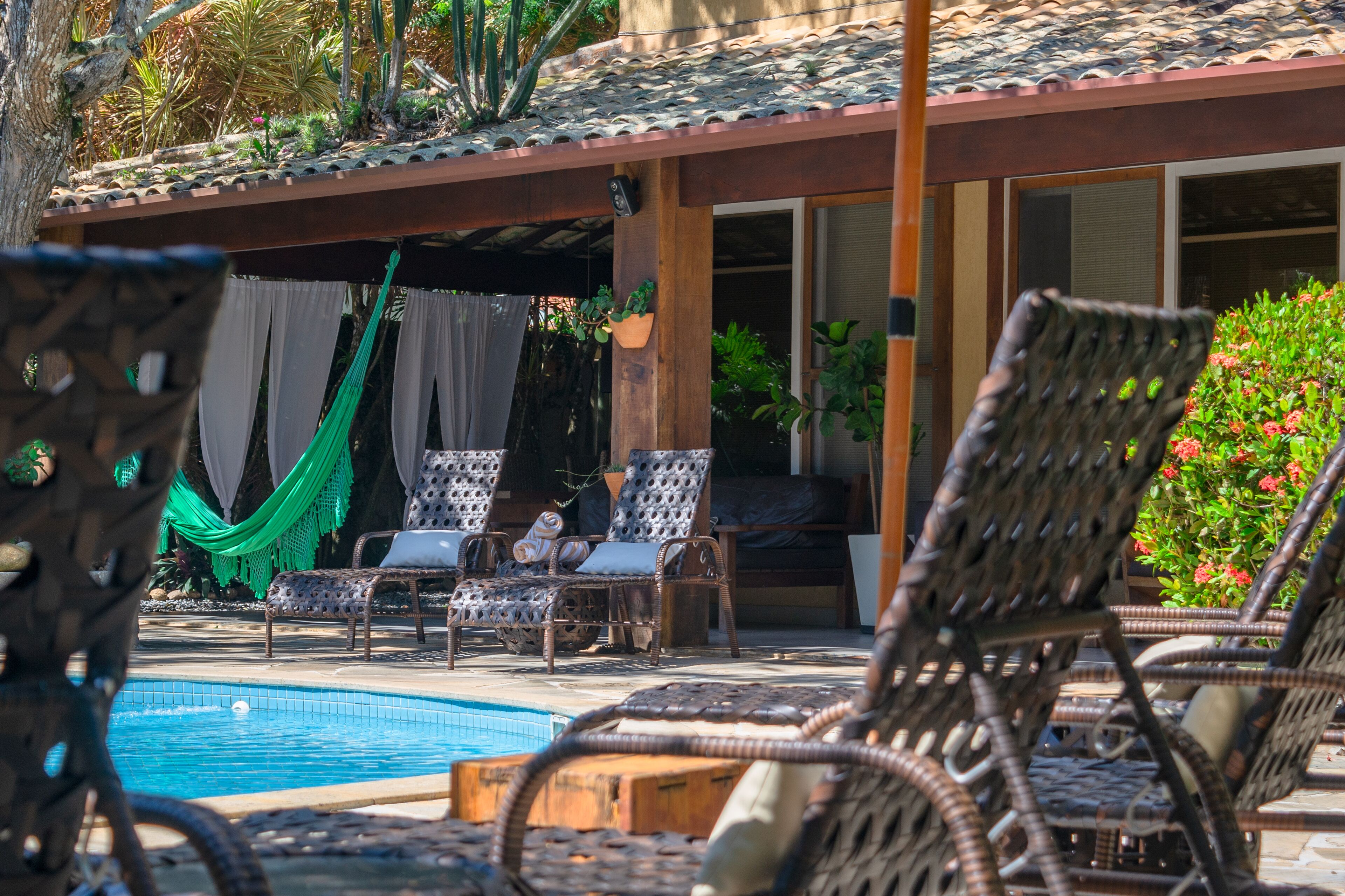 A poolside area with wicker lounge chairs, a hammock, and a tiled roof.