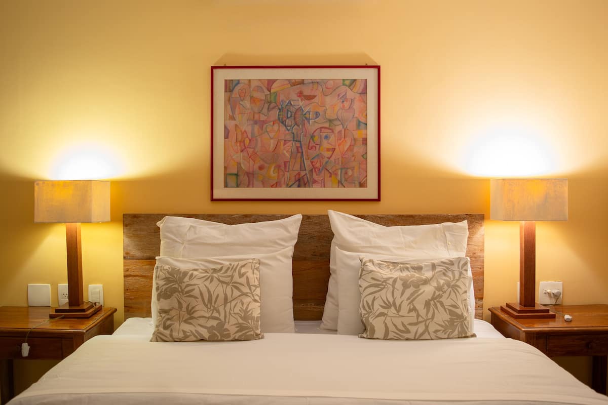 A hotel room with a large bed, two bedside tables with lamps, a wooden headboard, and a framed abstract painting on the wall.
