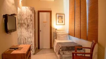 A bedroom with a bed, a wooden chair, a desk with a television, and a wall-mounted air conditioner.