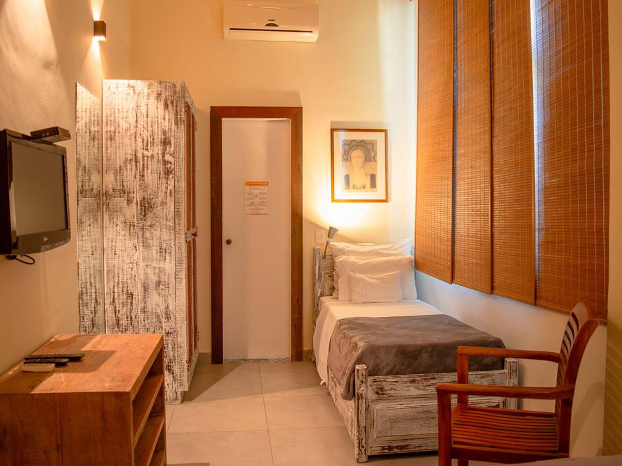 A bedroom with a bed, a wooden chair, a desk with a television, and a wall-mounted air conditioner.