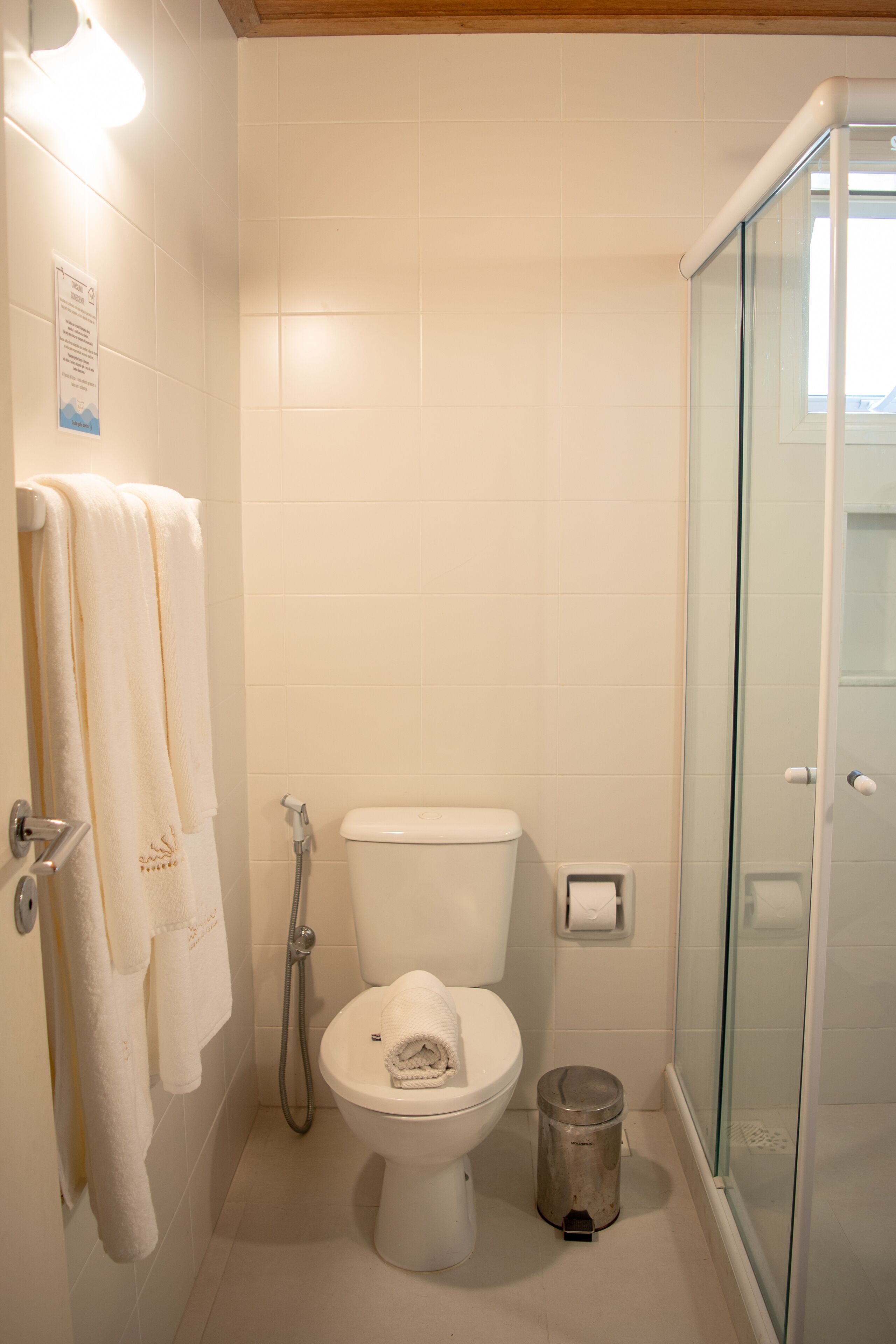 A bathroom with a toilet, a glass shower enclosure, and a trash can.