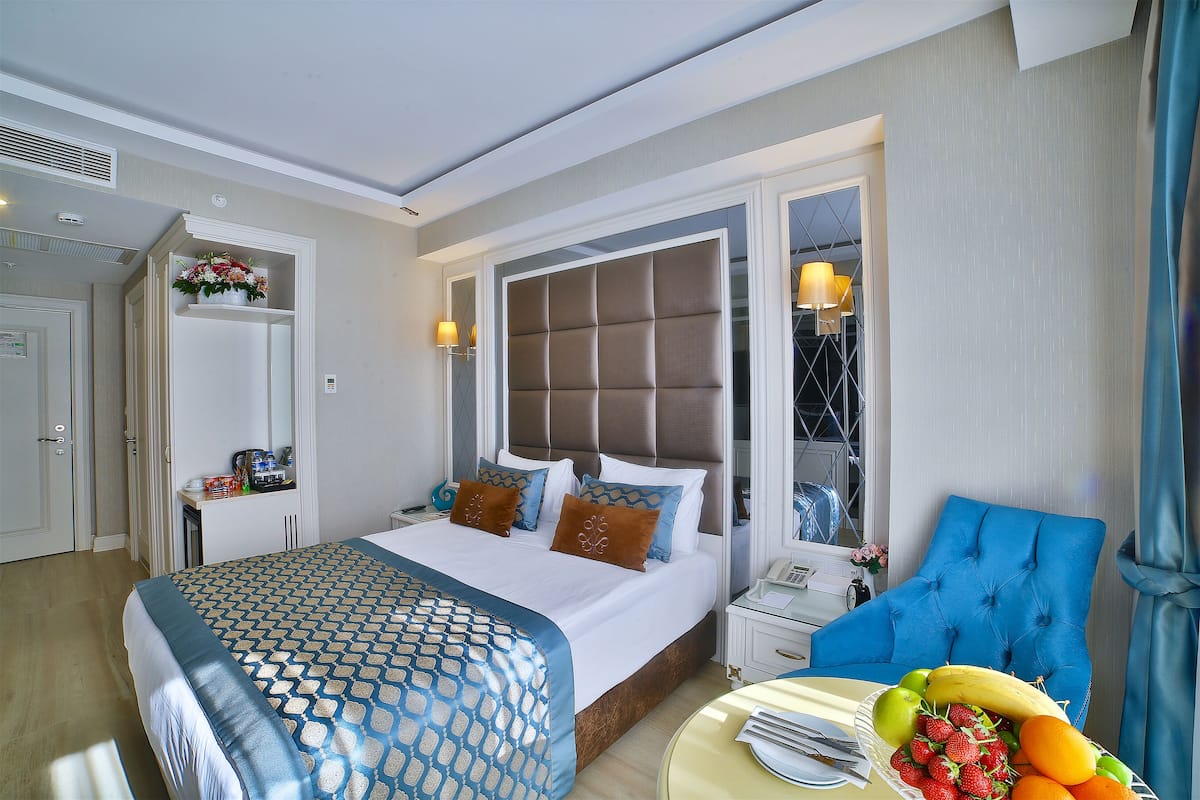 A hotel room with a large bed, a blue armchair, a bedside table with a lamp, and a fruit bowl.