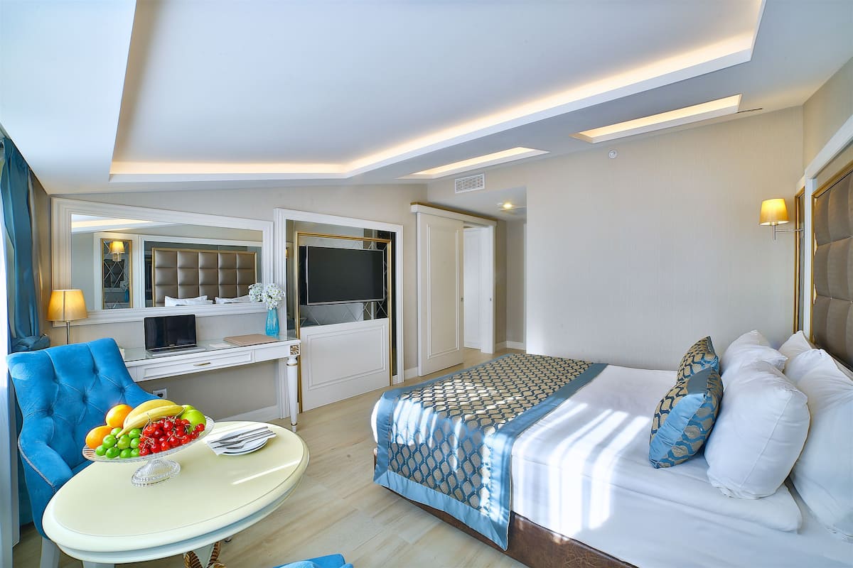A hotel room with a bed, a desk, a chair, and a table with fruit.