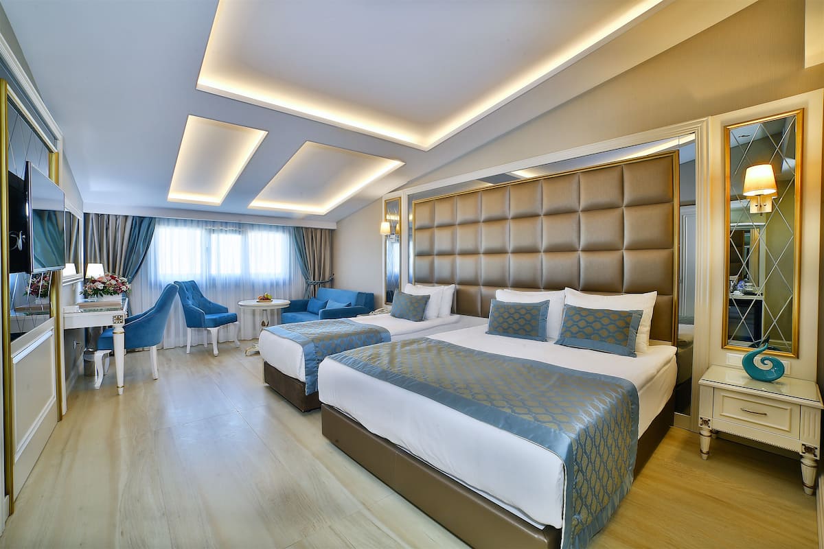 A hotel room with two beds, a sitting area with a sofa and chairs, a TV, and a mirror with a decorative item.