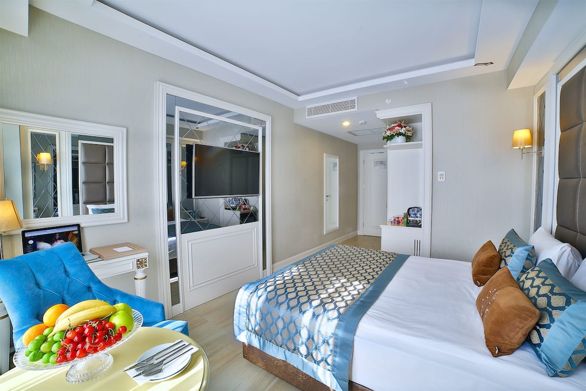 A hotel room with a bed, a chair, a dining table with fruit, a TV, and a wardrobe.