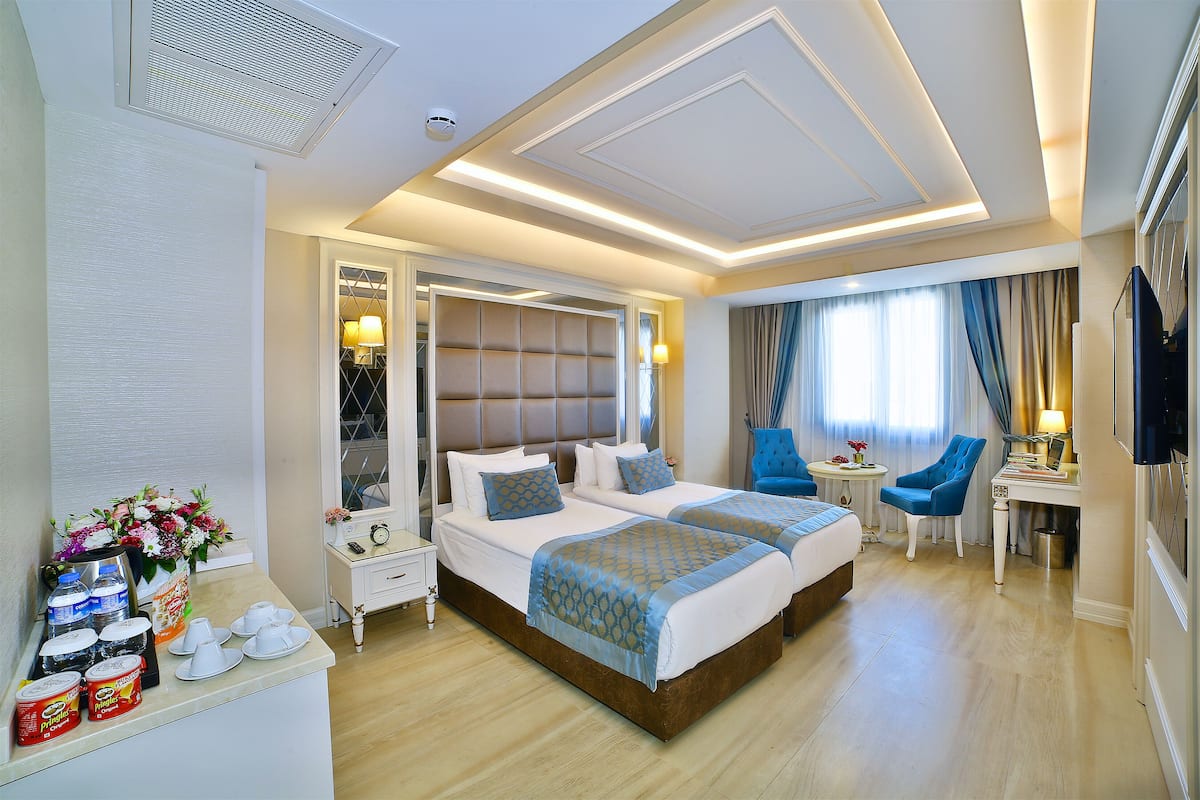 A hotel room with two beds, a desk, a chair, a TV, and a small table with a lamp.