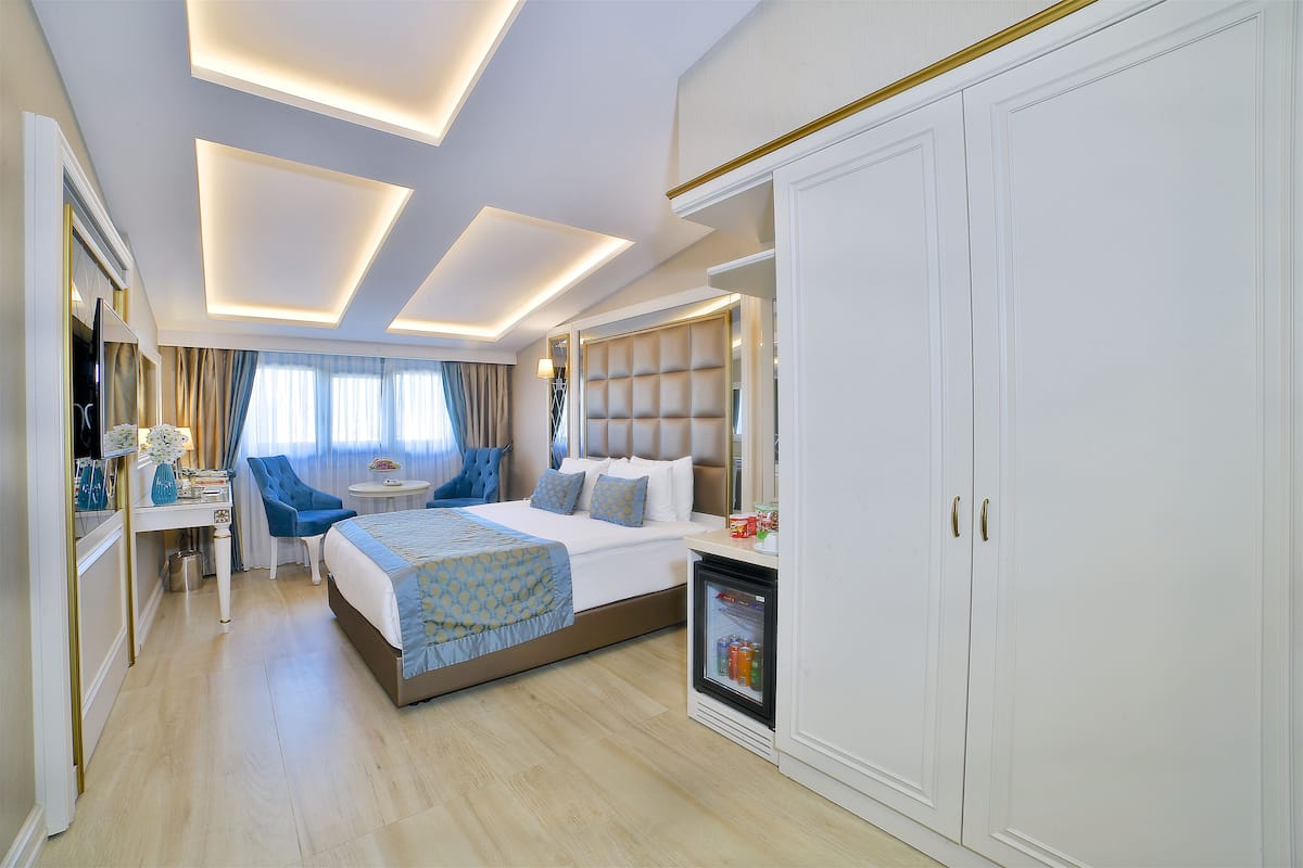 A hotel room with a bed, a desk, a chair, a wardrobe, and a minibar.
