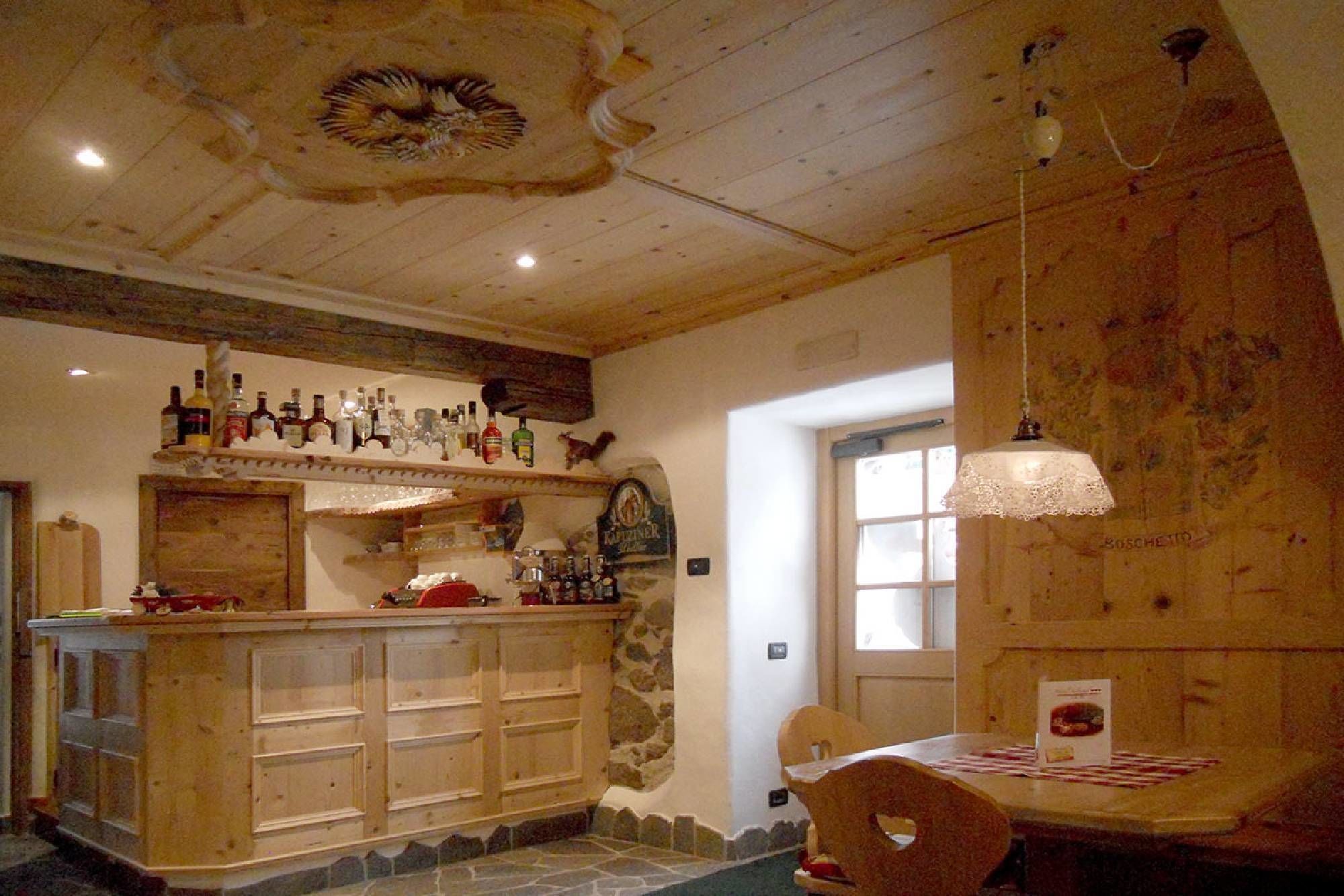 Un'accogliente area bar con scaffali in legno pieni di bottiglie, una parete in pietra e un soffitto in legno dal design particolare.