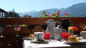 A table set for breakfast with a mountain view, including a teapot, cups, and a slice of cake. - HOTEL SALVANEL BOSCHETTO ROLAND DI DAPRA’ MARIA MADDALENA (Cavalese)