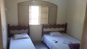 Een kleine, eenvoudige kamer met twee eenpersoonsbedden, een raam met zonwering en een betegelde vloer.