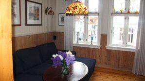 A room with a dark blue sofa, a wooden floor, a round wooden table with a vase of flowers, and a stained glass lamp. - Center Villa (Bergen)