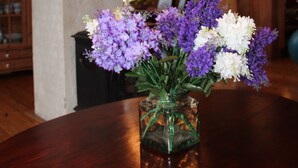 A wooden dining table with a glass vase containing purple and white flowers. - Center Villa (Bergen)