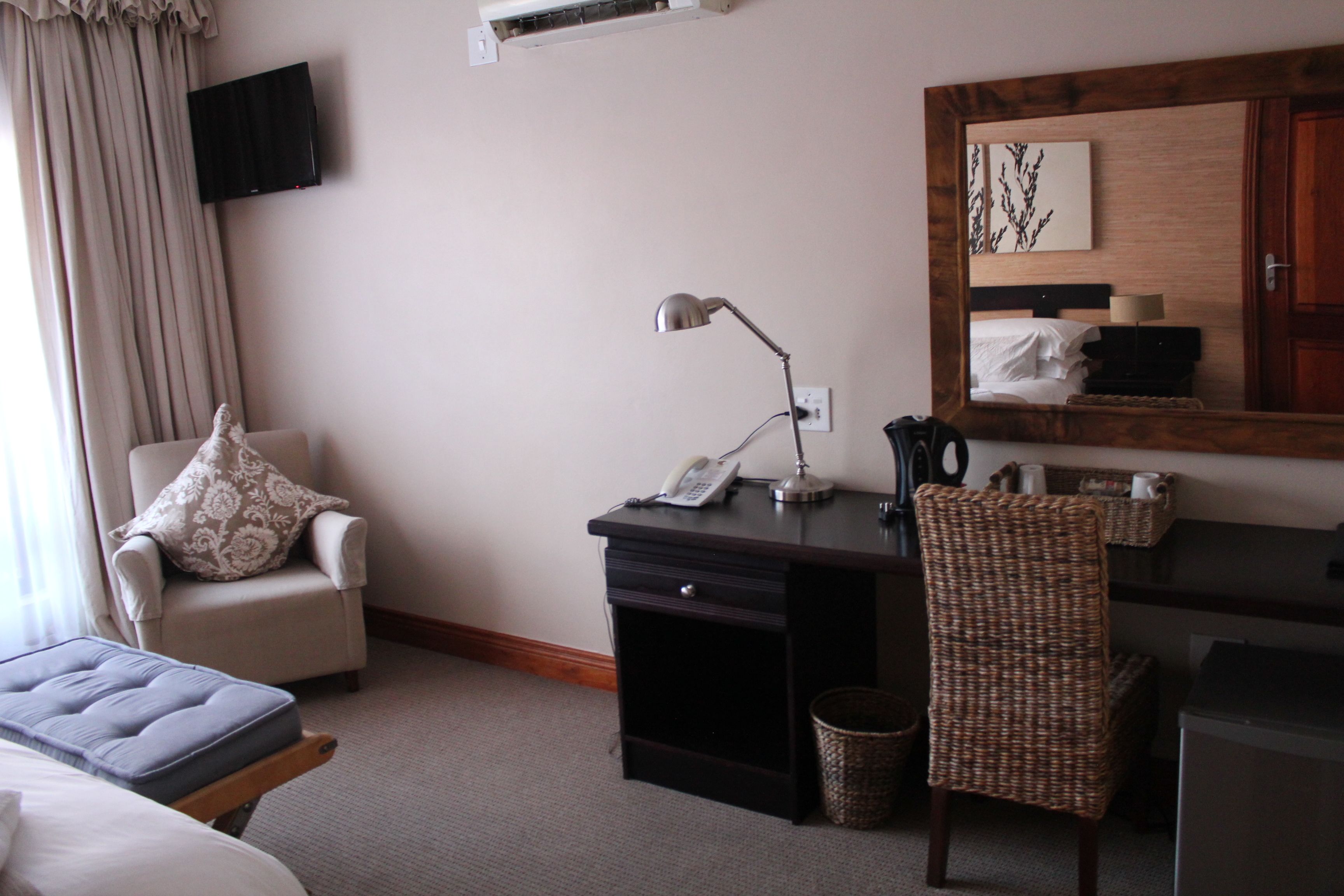 Une chambre d’hôtel avec un lit, un bureau avec une lampe, une chaise, un téléviseur fixé au mur et une tête de lit en bois.