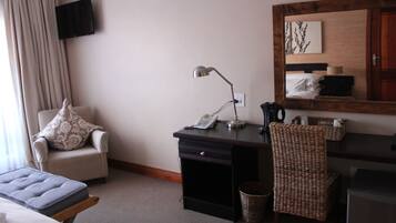 Une chambre d’hôtel avec un lit, un bureau avec une lampe, une chaise, un téléviseur fixé au mur et une tête de lit en bois.